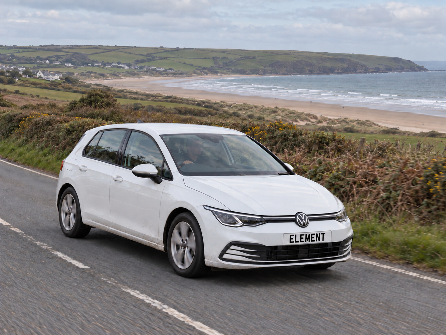 White Volkswagen Golf with ELEMENT number plate on a North Devon-inspired coastal road